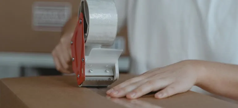 A person sealing a moving box