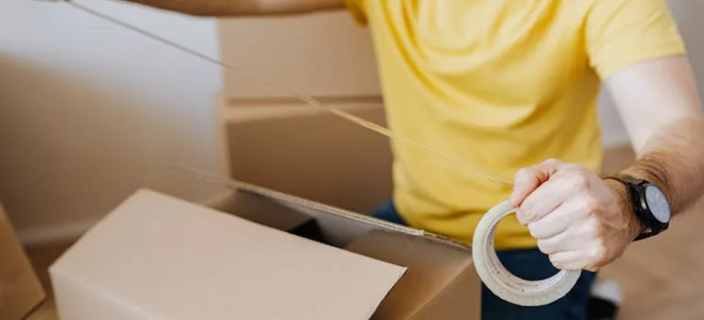 A person sealing a moving box