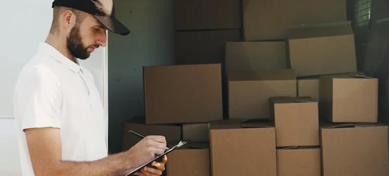 A mover using a checklist for moving from DC to Florida and loading boxes into the van