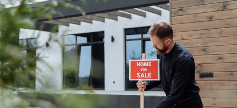 A man standing next to home for sale sign