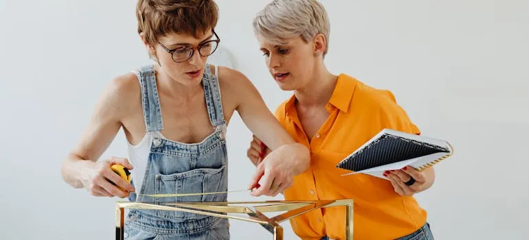 Two women measuring furniture in order to downsize your home when moving from DC to LA
