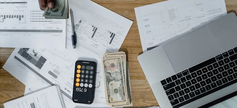 A person holding dollar bills and using laptop to research affordable vs luxury living in Virginia