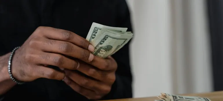 A person counting dollar bills and thinking should you move out of DC