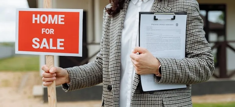 A person holding home for sale sign 