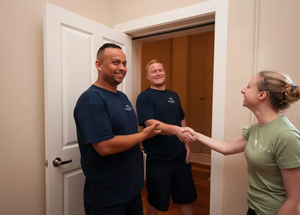 Two Beltway Movers crew members in navy shirts greeting a client at her front door