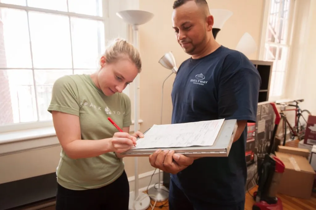Beltway Movers crew member holding a clipboard as a client reviews and signs moving paperwork.