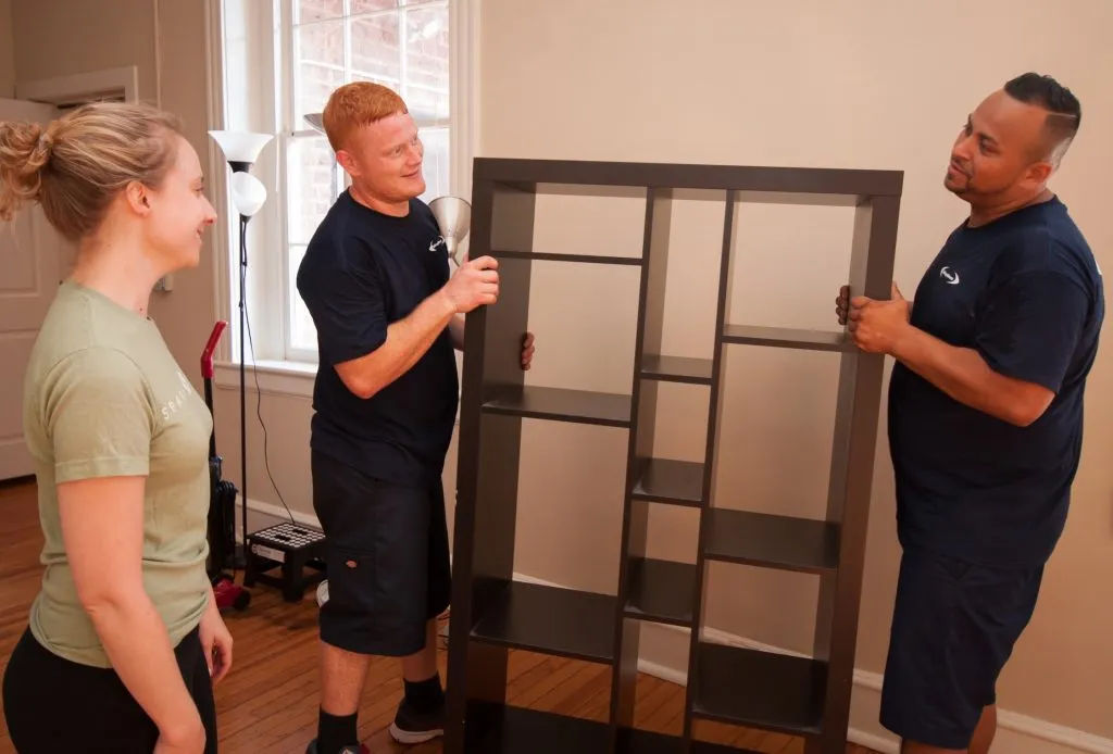 Two Beltway crew members positioning a tall black shelving unit as a client directs placement